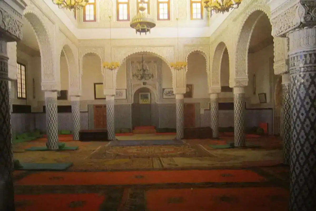Intérieur richement décoré du mausolée de Sidi Abdellah ben Hassoun à Salé, avec des lanternes suspendues, des murs en zellige et des arches sculptées.