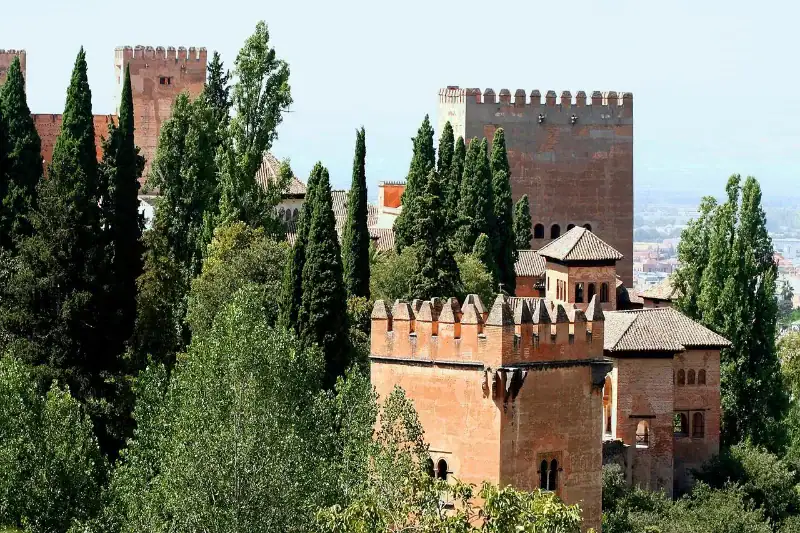 vue des tours fortifiées de lalhambra à grenade entourées de cyprès et dune végétation dense sous un ciel clair en andalousie