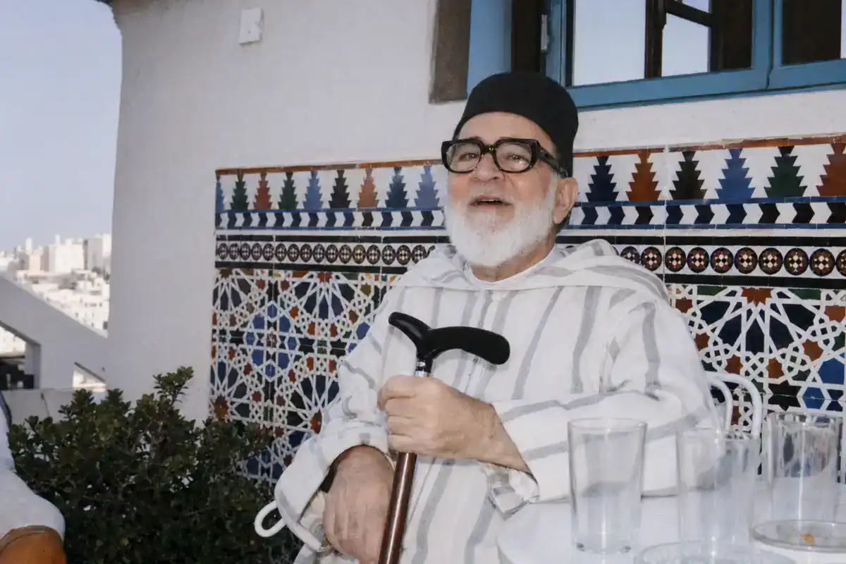 Portrait du Cheikh Abdallah ben Seddiq al-Ghoumari assis sur une terrasse à Tanger, portant une djellaba blanche et une chéchia noire.