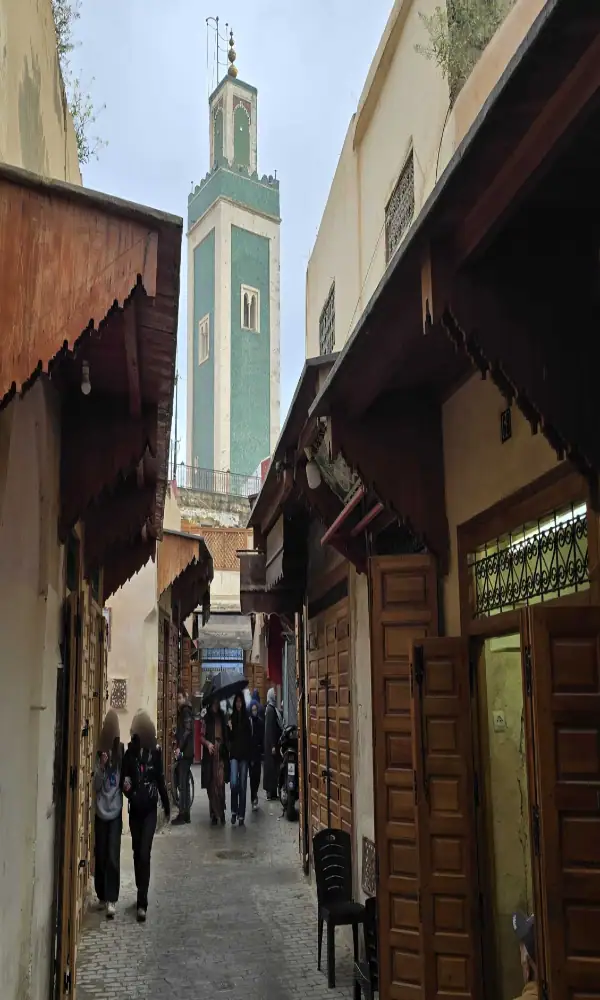 minaret vert en zelliges de la grande mosquée de meknès vue depuis une ruelle commerçante de la médina