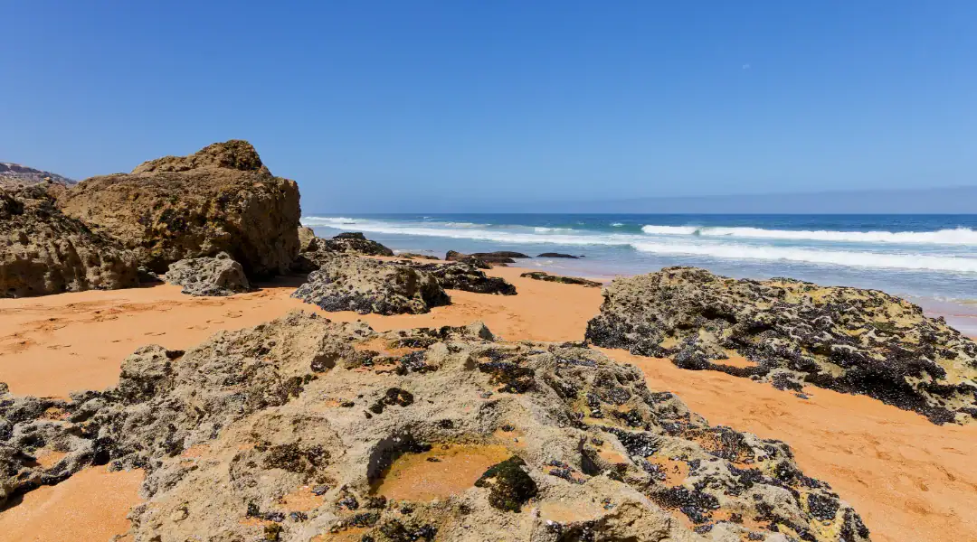 gros plan sur les rochers escarpés et le sable ocre de la plage lalla fatna sous un ciel bleu pur safi maroc