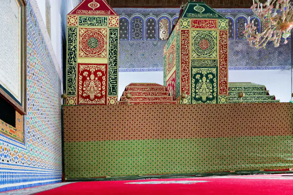 Intérieur du sanctuaire de Moulay Idriss Ier à Zerhoun montrant les catafalques ornés de broderies dorées et les murs en mosaïques zelliges.