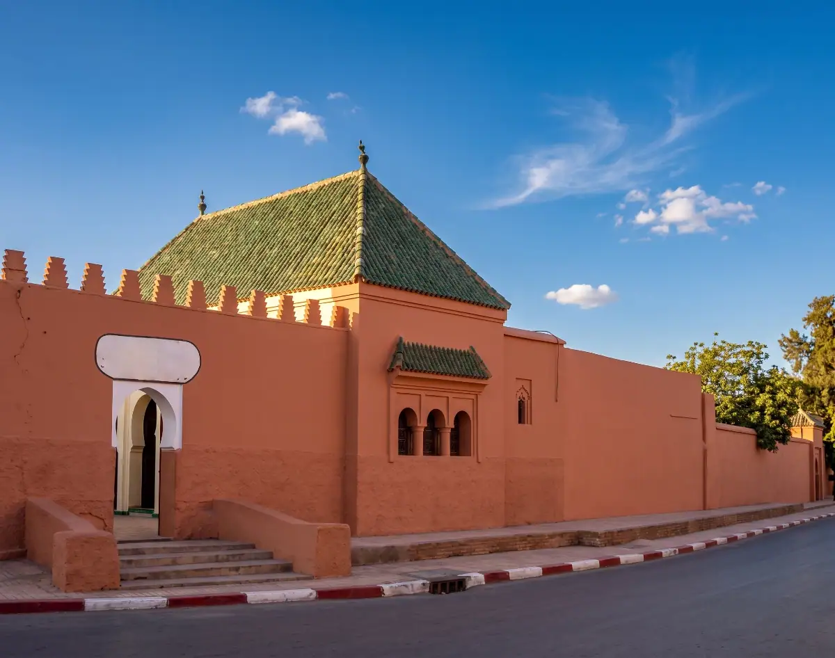 Vue extérieure du mausolée de Youssef Ben Tachfine à Marrakech, avec sa structure simple en pierre ocre et son dôme sous un ciel bleu.