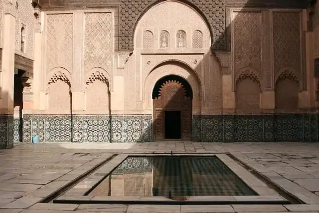 vue intérieure de la médersa ben youssef à marrakech montrant le bassin central la cour pavée de marbre et les façades ornées de zelliges et de bois de cèdre sculpté