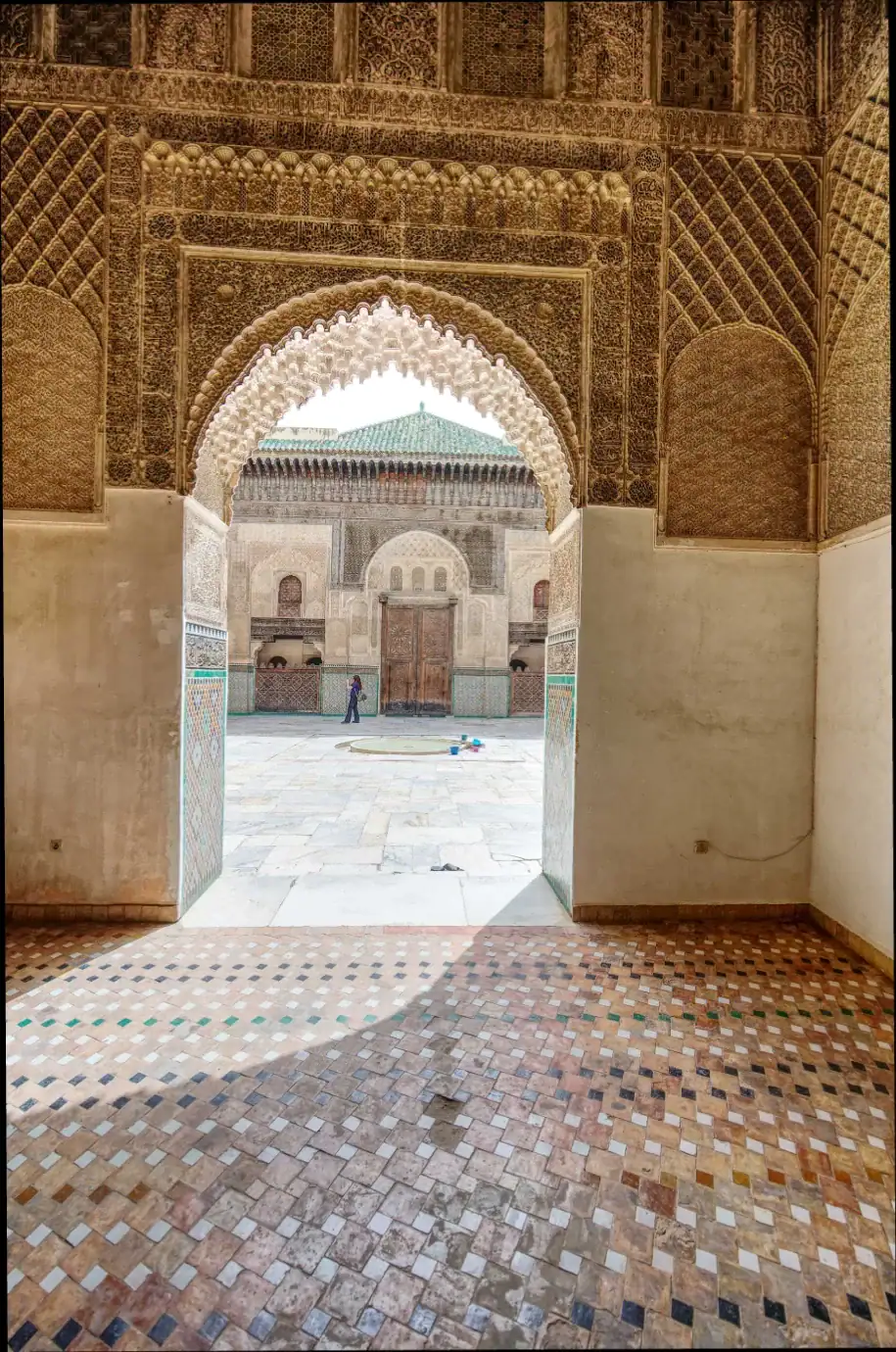 vue de la cour intérieure de la médersa bou inania à fès à travers une arcade de stuc sculpté