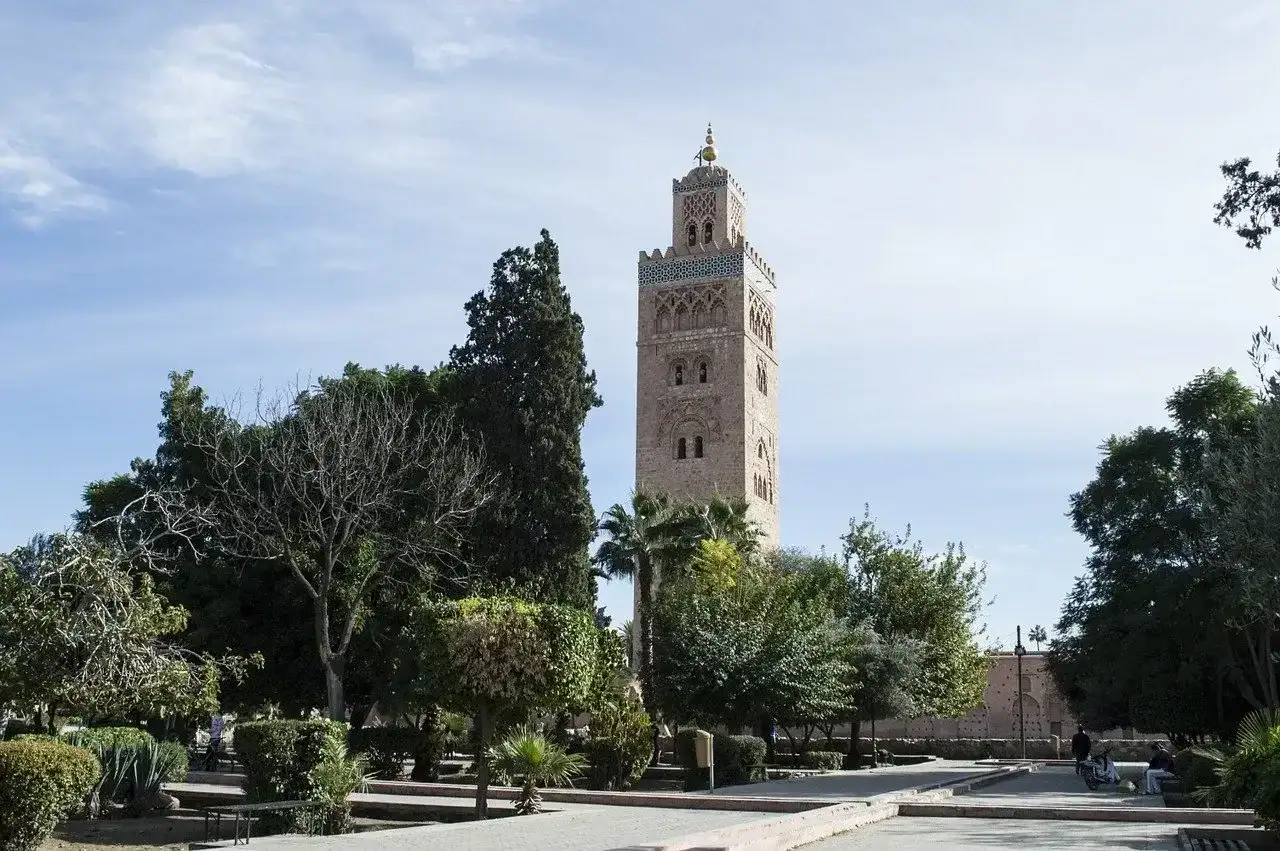 minaret de la mosquée de la koutoubia à marrakech entouré de jardins et de palmiers sous un ciel bleu