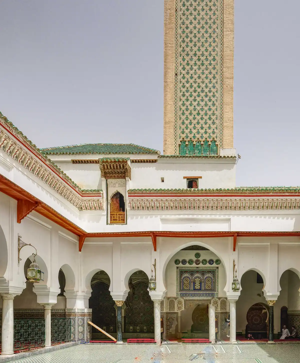 Vue panoramique du patio intérieur de la mosquée Moulay Idriss II à Fès, montrant le minaret orné, les arcades blanches et le sol en zelliges géométriques.