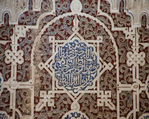 Détail d'une calligraphie arabe sculptée sur stuc avec des motifs d'entrelacs et de l'écriture bleue au centre, typique de l'architecture nasride en Espagne.