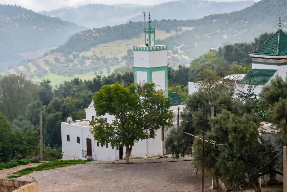 Vue sur le mausolée de Sidi Lahcen Lyoussi avec son minaret blanc et vert, niché au cœur d'un paysage de collines verdoyantes.