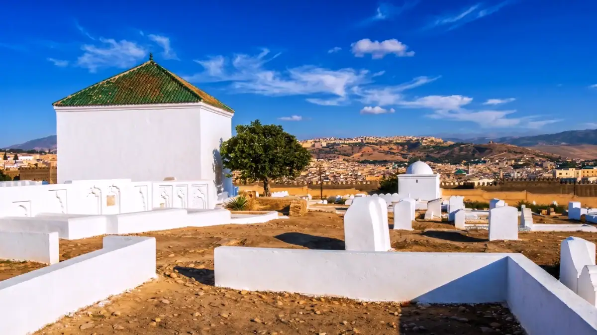 Vue du mausolée de al-Darras ibn Ismail situé dans le cimetière de Fès avec la médina en arrière-plan sous un ciel bleu.
