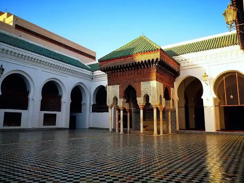 Cour en marbre et zelliges de l'université Al-Qarawiyyin à Fès avec son pavillon traditionnel en bois sculpté et arcs blancs.