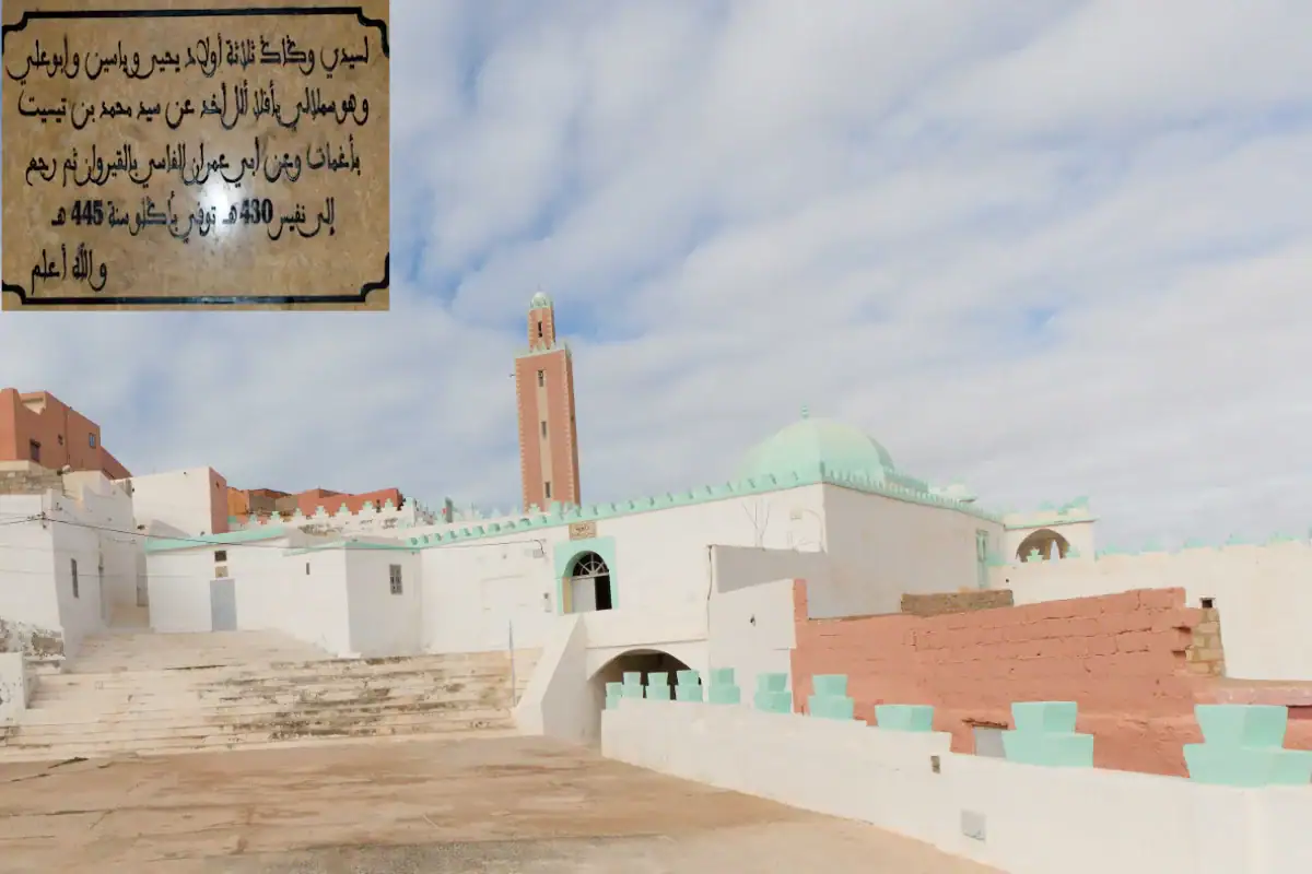 Vue extérieure blanche et verte de la zaouïa historique de Sidi Wagagg ibn Zallu à Aglou, avec son minaret et son dôme sous un ciel nuageux.