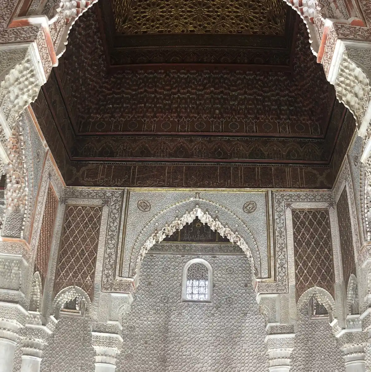 Vue intérieure détaillée des Tombeaux Saadiens à Marrakech, montrant la richesse de l'architecture avec ses murs en stuc finement sculpté, ses arcades décorées de calligraphies et son magnifique plafond en cèdre ouvragé.