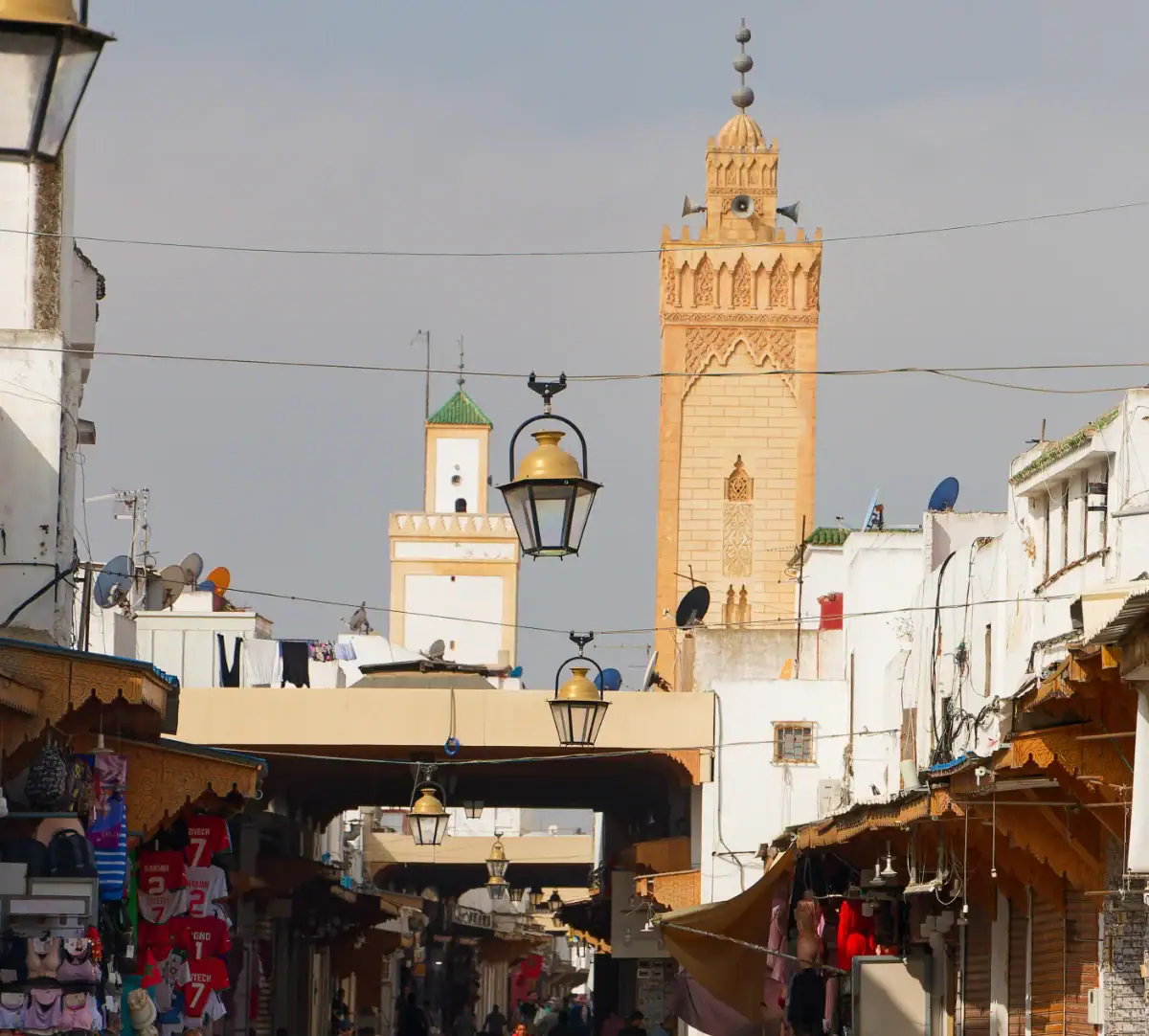 Rue animée de la médina de Rabat surmontée d'un minaret traditionnel en brique, symbole de l'architecture historique de l'Empire Almohade.