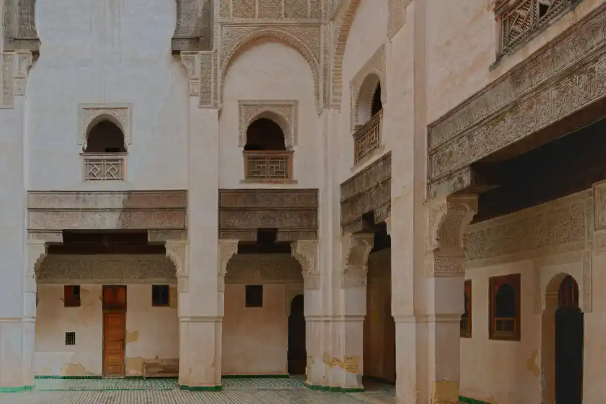 Vue détaillée de la cour intérieure de la Médersa Bou Inania à Fès, mettant en évidence les arcades sculptées en stuc, les fenêtres ornées de boiseries traditionnelles et le sol recouvert de zellige.